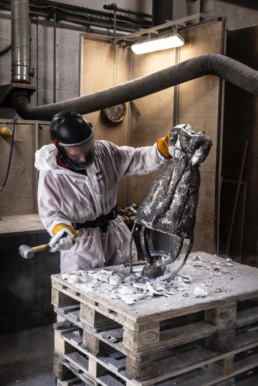 The torso of a metal statue, wearing a Victorian dress, goes through the construction process.