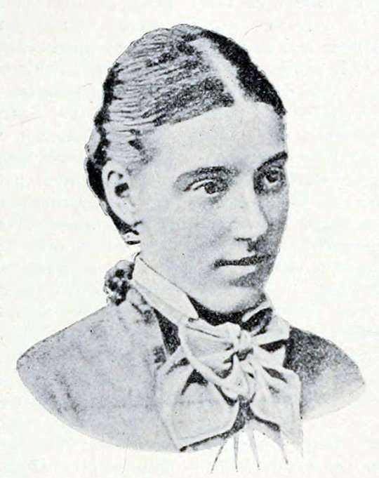 Grainy black and white portrait of Fanny Wilkinson, with her hair tied back and wearing a bow around her neck.