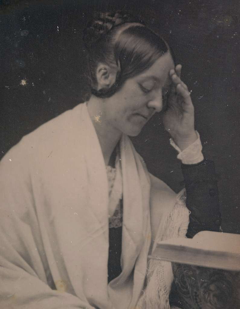 Monochrome photograph of Margaret Fuller, wrapped in a shawl, reading a book.