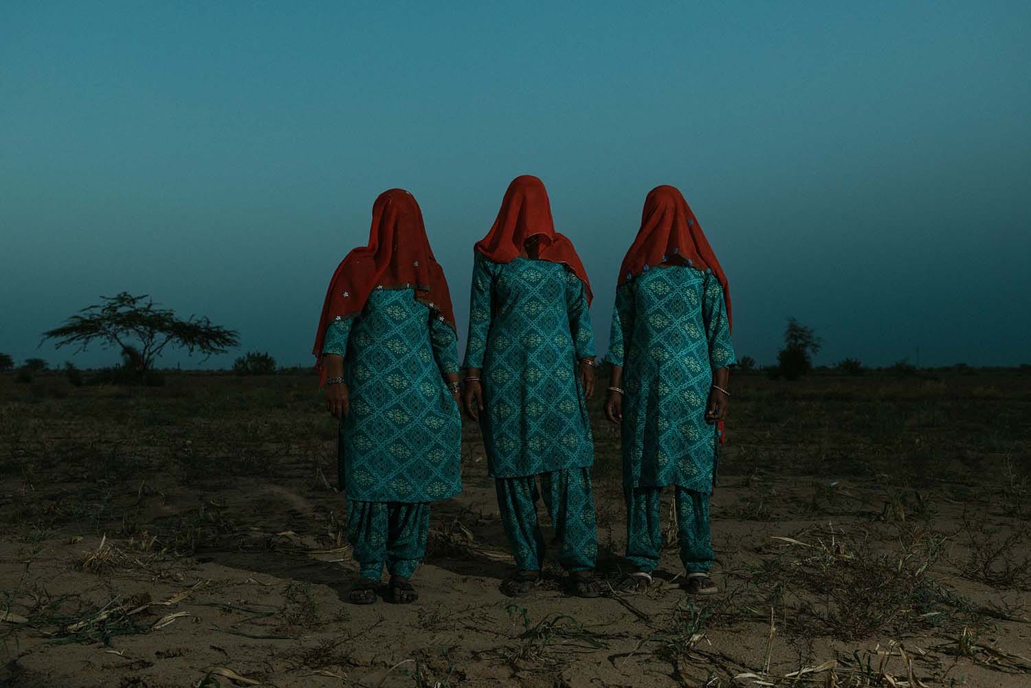 Three women stand in a line, their faces obscured by red scarves.