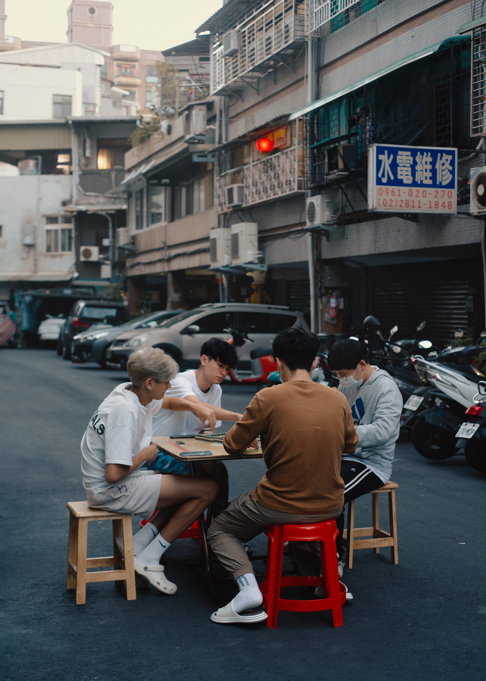 Four kids have set up a games table in the street. They sit on stools one on each side of a square table.