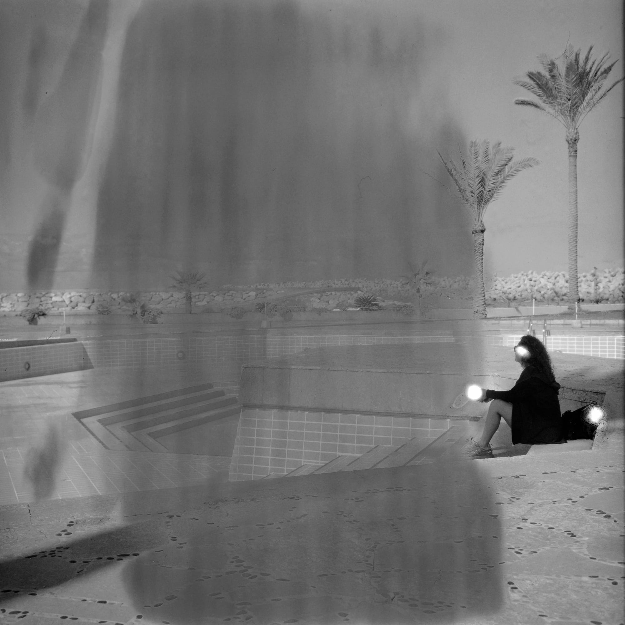 A woman sits in an outdoor seating area. Her face and hands are obscured. The photo is murky.