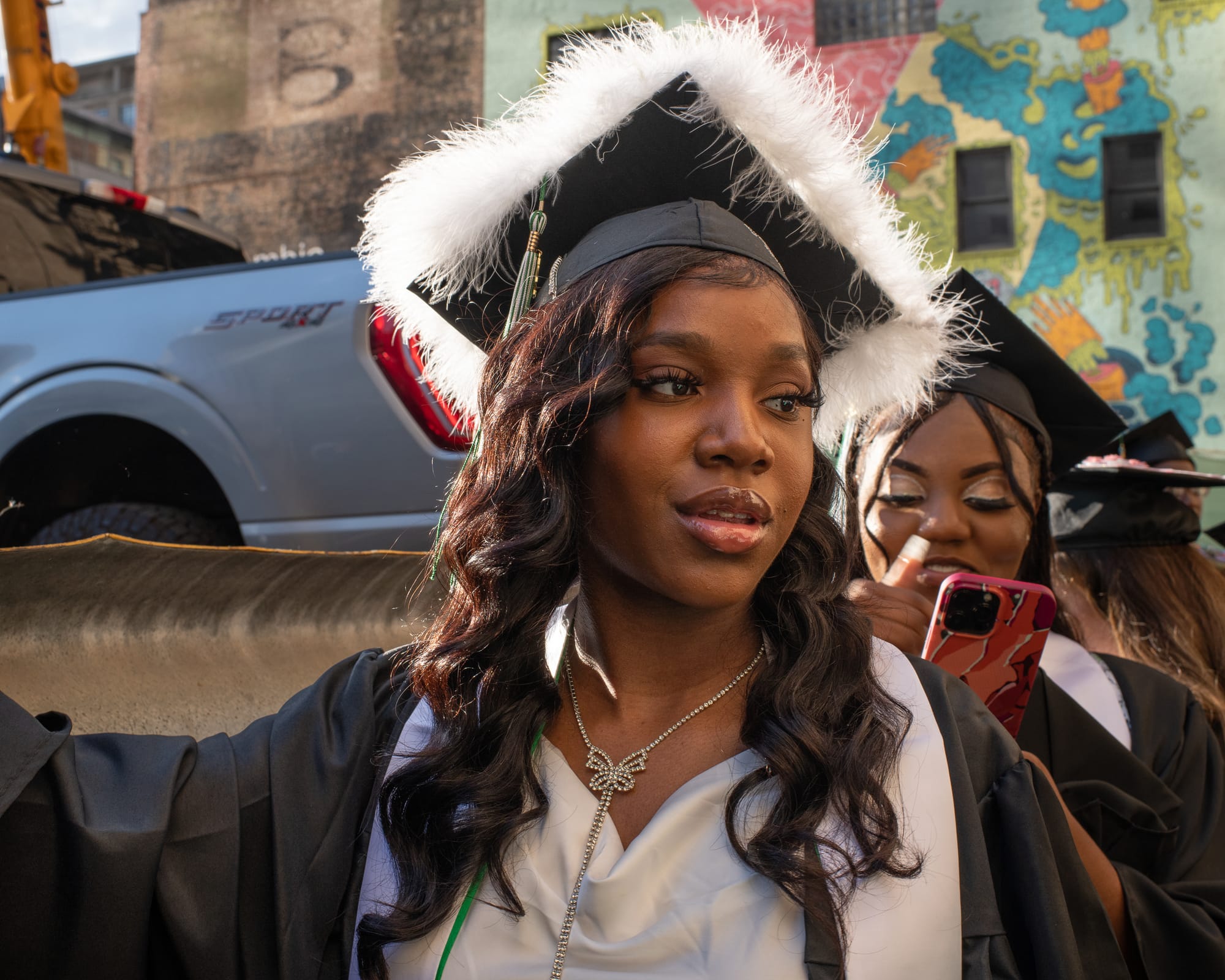 A woman dressed for graduation in a cap and gown. The cap is trimmed with white feathers.