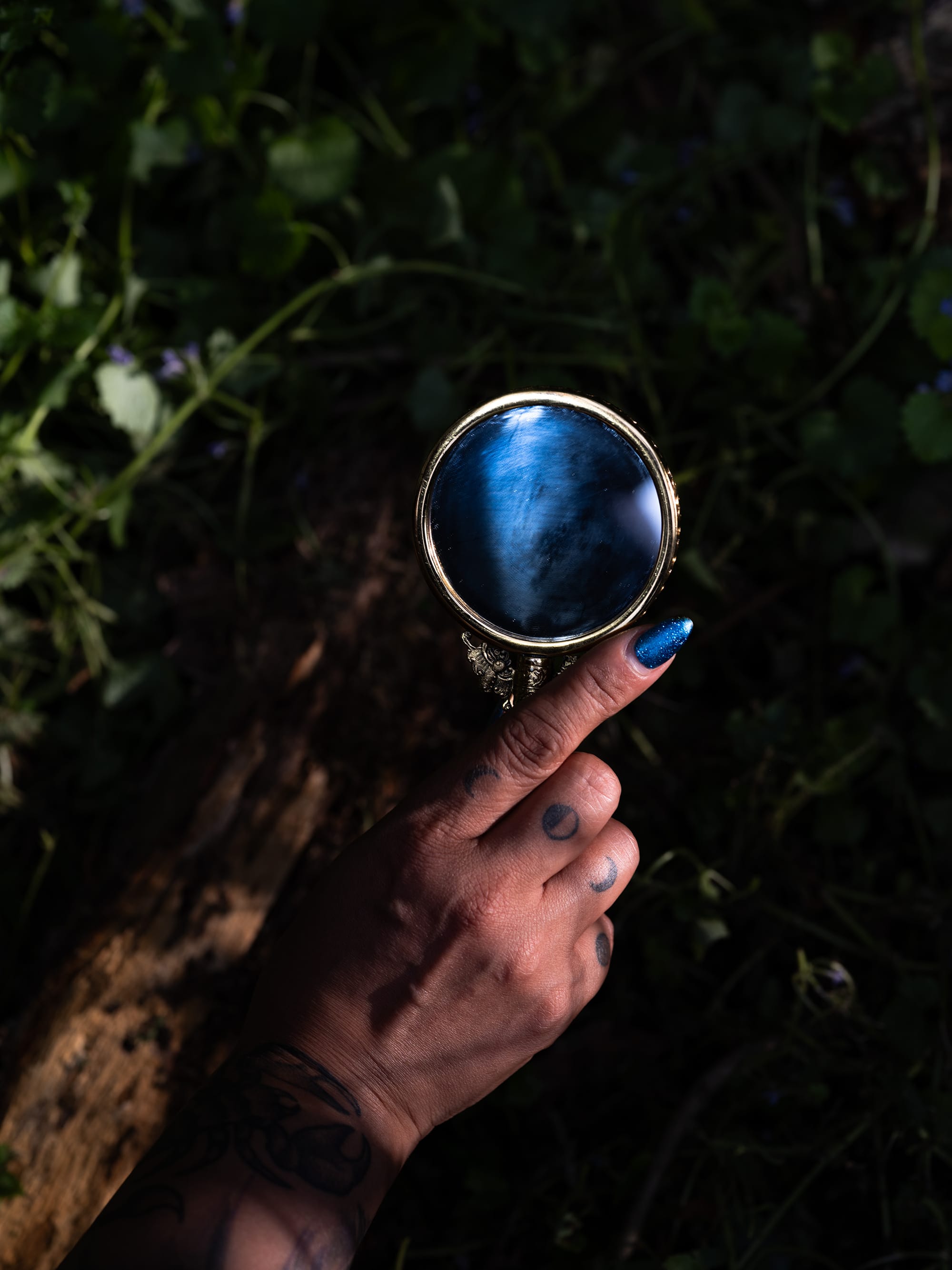 A hand with blue nail polish holds up what appears to be a blue-tinged magnifying glass.