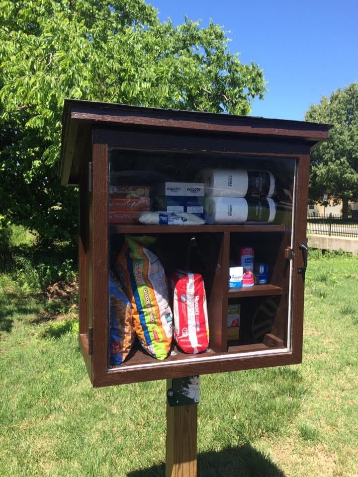 A wooden box with a clear glass door contains packaged foods and other household items.