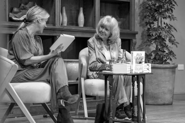 Black and white photograph showing a stage on which Jilly Cooper, facing the camera, and Jojo Moyes, in side profile, are talking.